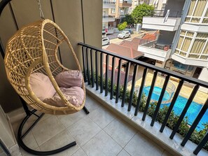 Ein Korbstuhl mit Kissen auf einem Balkon mit Blick auf einen Pool.