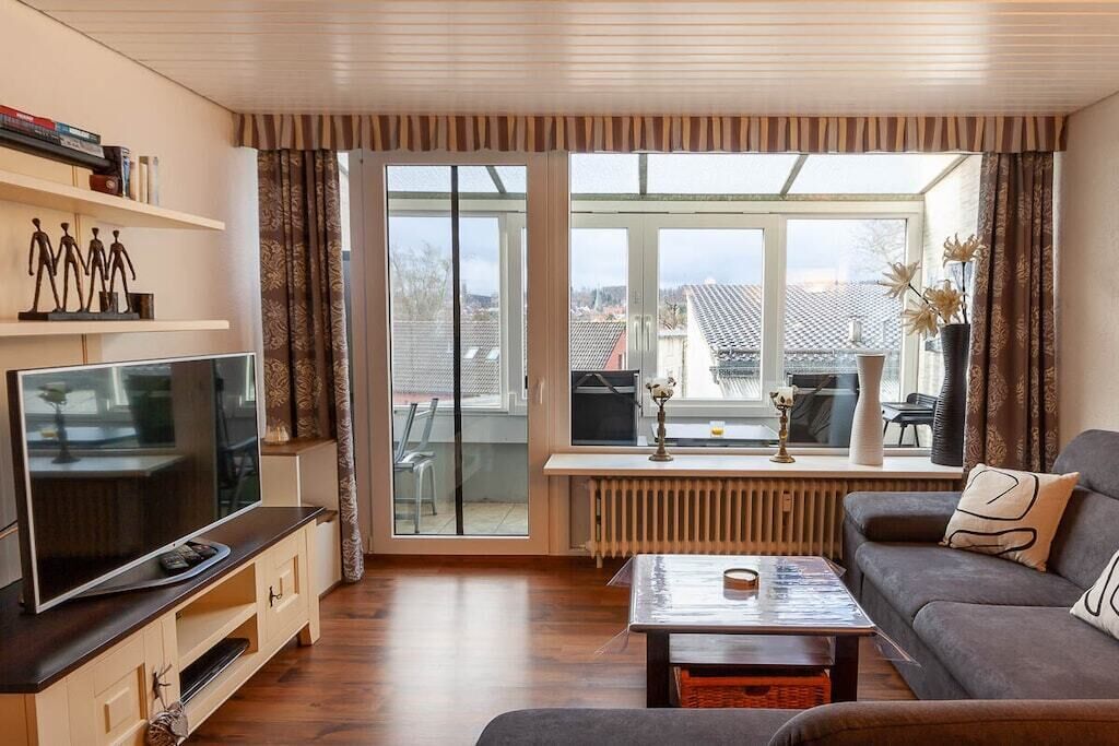 Un salon comprenant un téléviseur, un canapé, une table basse et une grande fenêtre avec des rideaux.