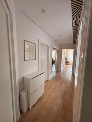 A hallway with white walls, a wooden floor, a white cabinet, and a framed picture.