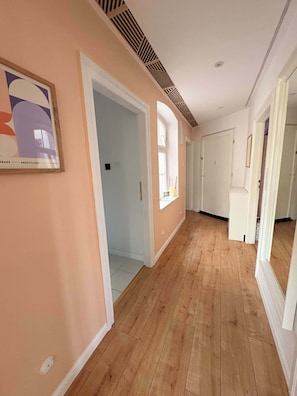 Un pasillo con suelo de madera, puertas blancas y una obra enmarcada en la pared.