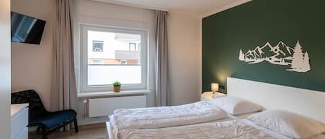 A hotel room with two beds, a TV, a window with curtains, and a wall decal.