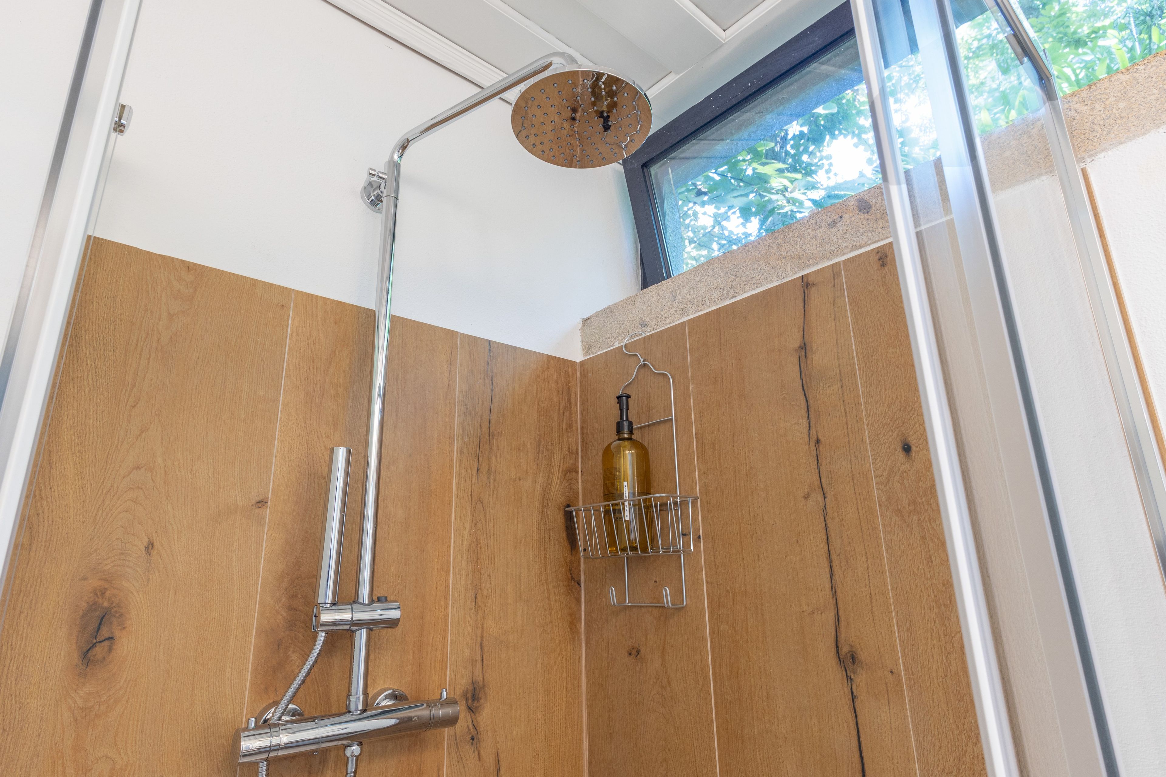 Une douche avec un mur en panneaux de bois, une porte en verre et une bouteille de shampoing.