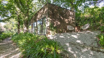 Un rustico chalet con una finestra a vetro, immerso nel verde e con un vialetto sterrato.