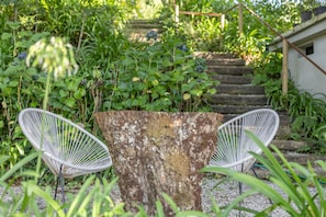 A garden with two white wire chairs, a large tree stump, and a staircase surrounded by greenery. - 'Suite Alfazema' Room with Shared Pool and Private Garden (Fornelos)