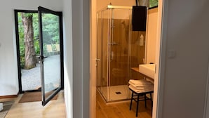 Ein modernes Badezimmer mit Duschkabine aus Glas, einer Holzbank und Blick ins Freie durch eine Glastür.