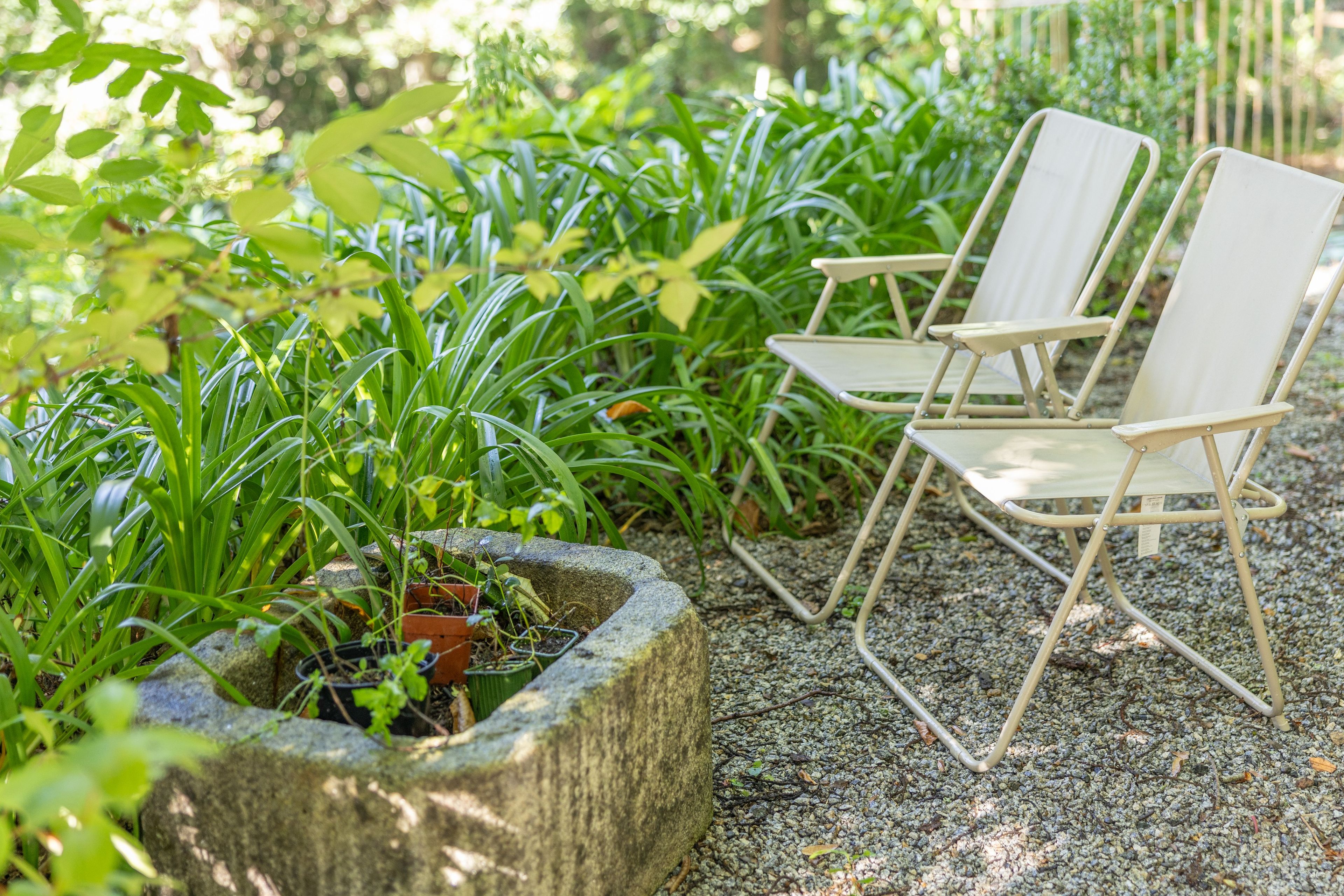 Un jardín con dos sillas blancas plegables y una jardinera de piedra con diversas plantas.