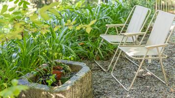 Un jardín con dos sillas blancas plegables y una jardinera de piedra con diversas plantas.