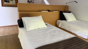 Ein Zimmer mit zwei Betten, einem Holzkopfstück, einem gerahmten Bild an der Wand und einer kleinen Ablage mit Büchern und einer Schale.