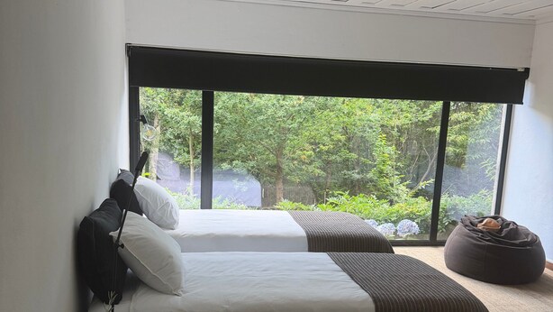 Ein modernes Schlafzimmer mit großem Fenster, einem Bett mit weißer und gestreifter Bettwäsche, einem Nachttisch mit Lampe und einem Sitzsack.