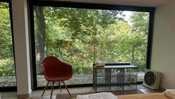 A room with a bed, a red chair, a small table with a towel, and a window with a view of trees. - Suite Camélia Room with Shared Pool and Private Garden (Fornelos)