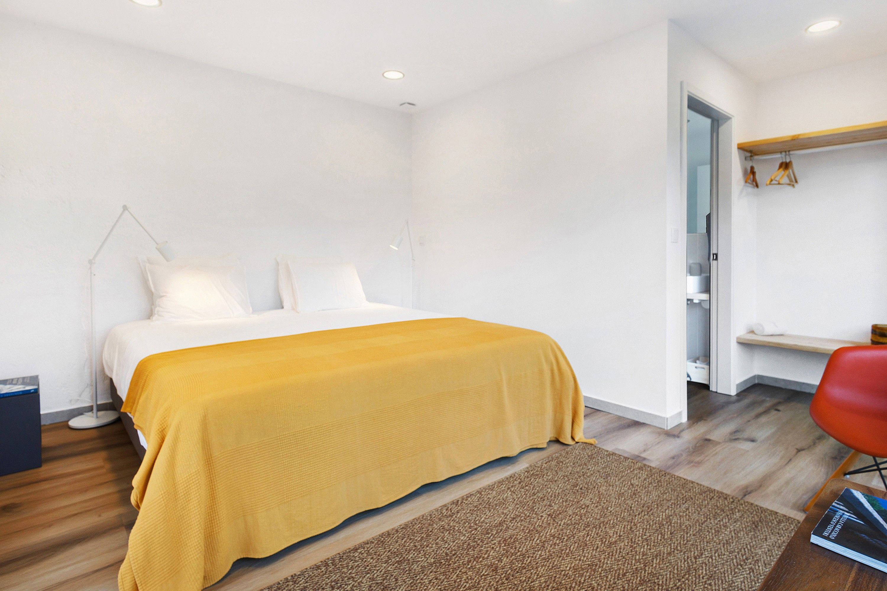 A modern bedroom with a bed, a bedside lamp, a red chair, and a wooden floor.