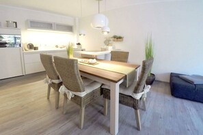 Eine moderne Küche mit weißen Schränken, einem Holztisch, Korbstühlen und Pendelleuchten.