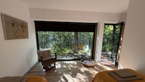 Une chambre avec deux lits, une chaise, une fenêtre donnant sur des arbres et un tableau accroché au mur.