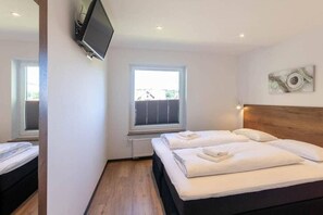 A hotel room with a bed, a television mounted on the wall, and a window with blinds. - Mountain view with balcony (Braunlage)