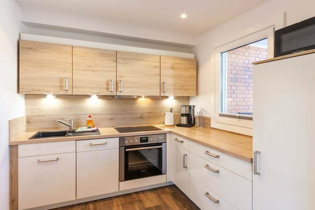 Une cuisine moderne avec des meubles en bois, un four encastré, un évier et une fenêtre donnant sur un mur de briques.