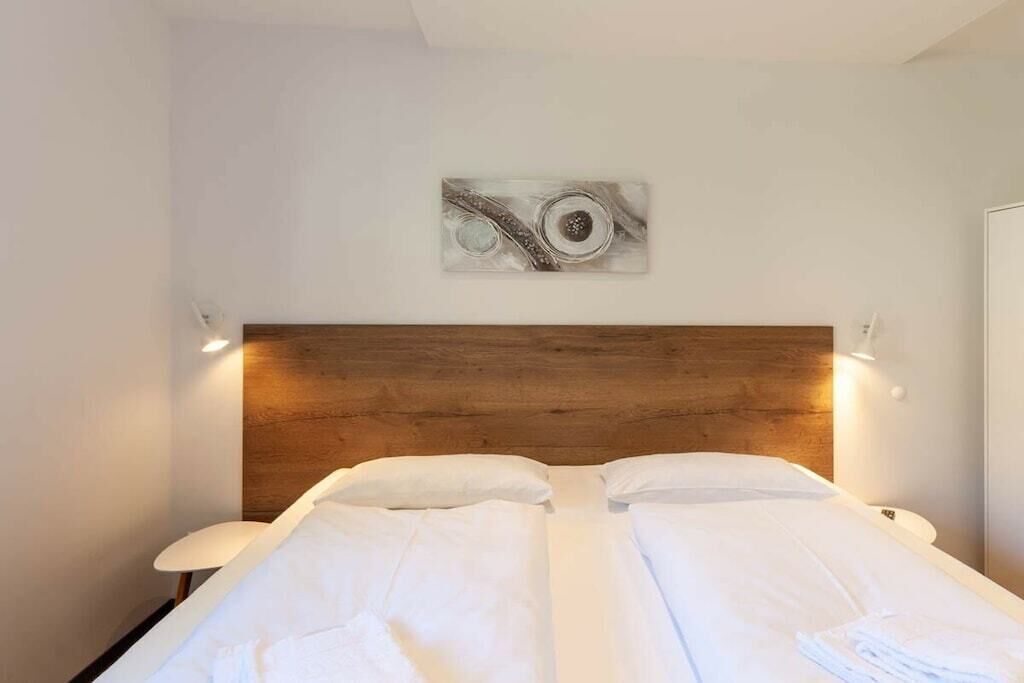 Ein Hotelzimmer mit einem hölzernen Kopfteil, einem Gemälde über dem Bett und einer weißen Tagesdecke.