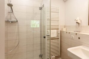 A bathroom with a glass-enclosed shower, a white sink, and a towel rack. - Mountain view with balcony (Braunlage)