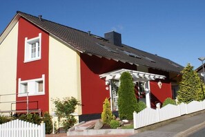 Una casa a due piani con facciata rossa e gialla, un portico bianco e una recinzione di legno bianco.