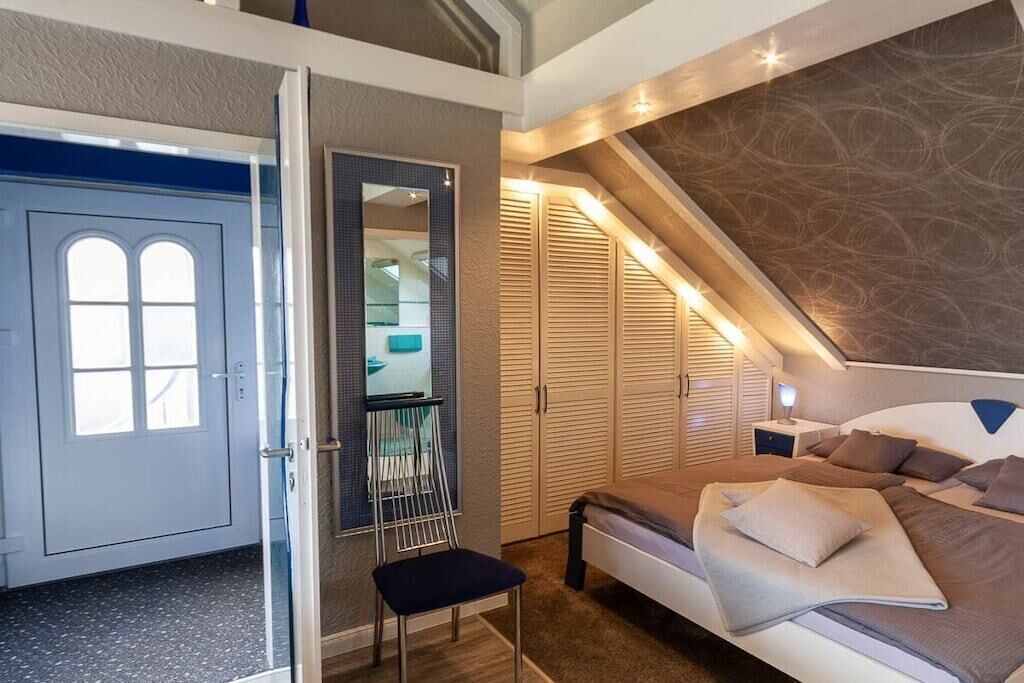 A bedroom with a bed, a chair, a wardrobe, and a door.