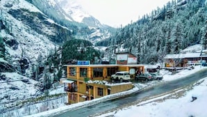 Un immeuble à étages, une route devant, et des montagnes enneigées en arrière-plan.