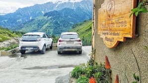 Señal de 'The Apple Tree Lodge & Cafe Kothi Manali' con dos coches estacionados en la parte delantera.