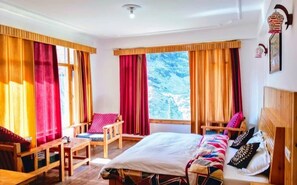 Una habitación con cama, dos sillas, una mesita y ventanas grandes con cortinas.