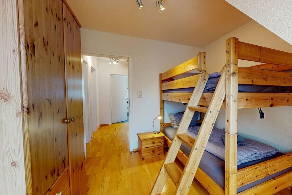Un lit superposé avec une échelle, une armoire en bois et une petite table de chevet avec une lampe.