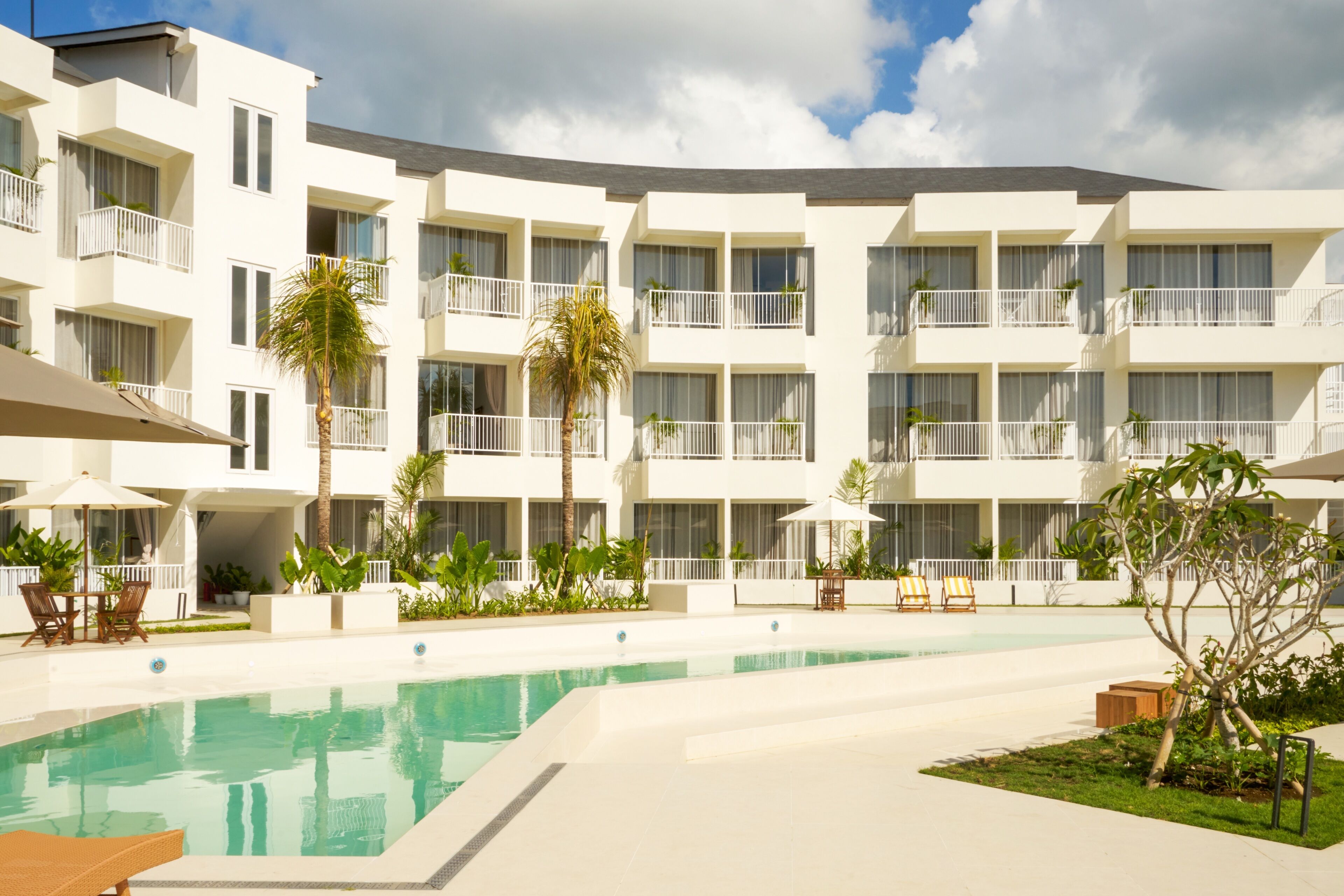 A modern hotel with a swimming pool, multiple balconies, and outdoor seating areas.