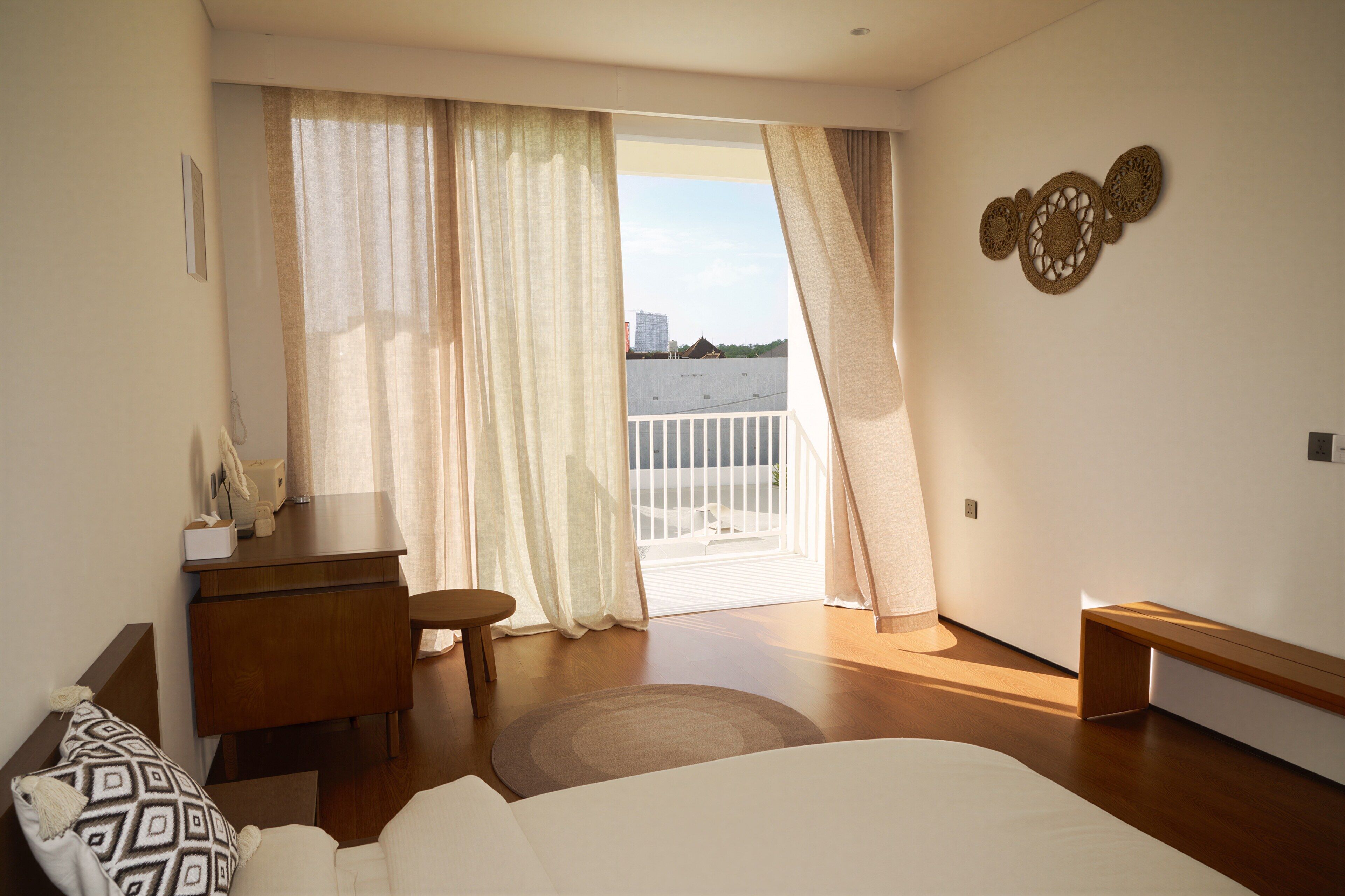 A hotel room with a bed, a desk, a chair, a small table, and a balcony with a view of the city.