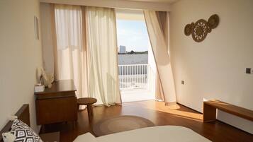 A hotel room with a bed, a desk, a chair, a small table, and a balcony with a view of the city.