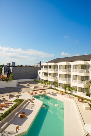 A hotel with a swimming pool, lounge chairs, and a modern building with balconies. - O.Serendipity Kuta (Kuta)