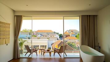 A spacious living room with a large sliding glass door leading to a balcony, a modern bathtub, and two wicker chairs.