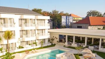 A hotel with a swimming pool, outdoor seating, and a building with balconies.