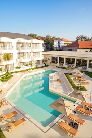 Un hotel con piscina, mobiliario exterior y un edificio con balcones.