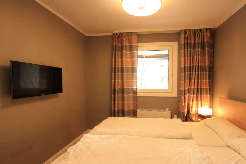 A hotel room with a bed, a television mounted on the wall, and curtains on the window.