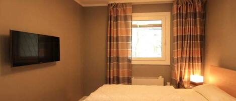 A hotel room with a bed, a television mounted on the wall, and curtains on the window.