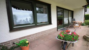 Una casa con un patio, un carriole con fiori e una sedia.
