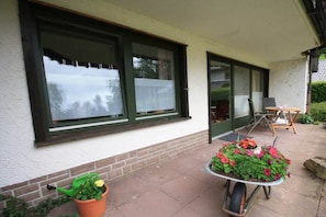A house with a patio area, a wheelbarrow with flowers, and a chair. - Holiday apartment with 2 bedrooms (Braunlage)