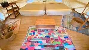 Interior de uma tenda com um colchonete acolchoado, um banco de madeira e uma cesta de vime.