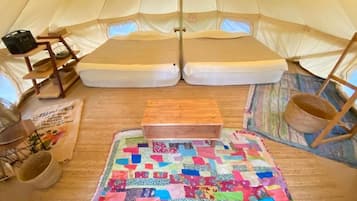 Een tent van binnen, met een gewatteerde vloermat, een houten bankje en een gevlochten mand.