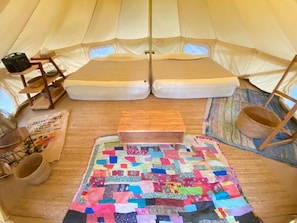 A tent interior with a quilted floor mat, a wooden bench, and a woven basket. - Rainbowforest (ishigaki)