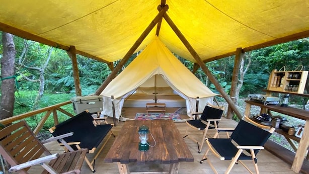Um deck de madeira com uma mesa e cadeiras no centro, rodeado por uma estrutura de toldo amarelo.