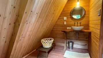 Een houten interieur met een schuine kap, een ronde spiegel, een wastafel en een klein krukje.