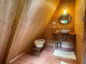 A wooden interior with a sloped ceiling, a round mirror, a sink, and a small stool. - Rainbowforest (ishigaki)