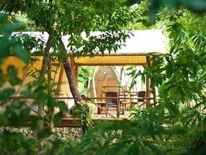 A wooden deck with a table and chairs, surrounded by greenery. - Rainbowforest (ishigaki)