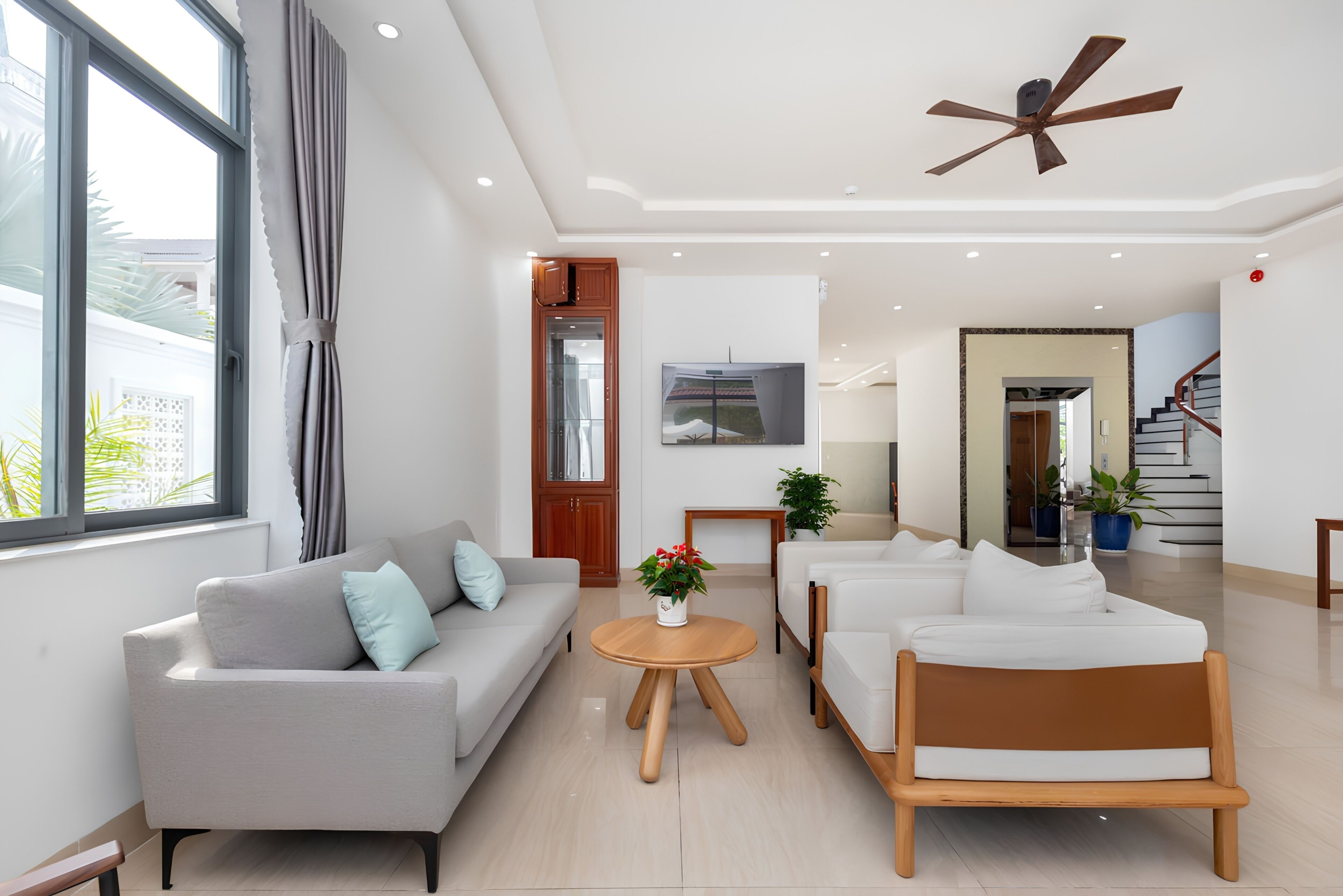 A modern living room with a sofa, armchairs, a coffee table, and a ceiling fan.