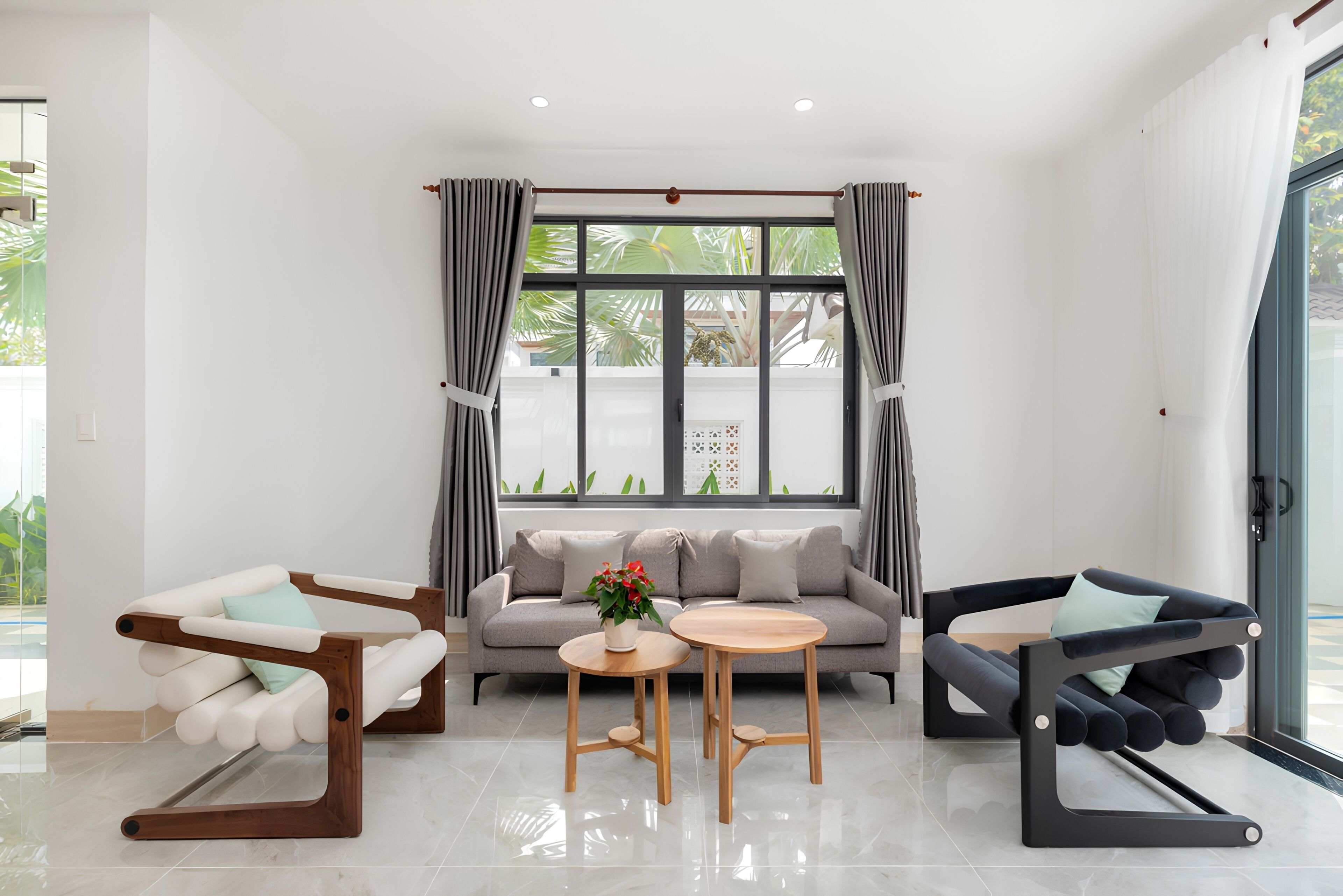 Un salon moderne avec un canapé, deux fauteuils, une table basse et une fenêtre avec des rideaux.