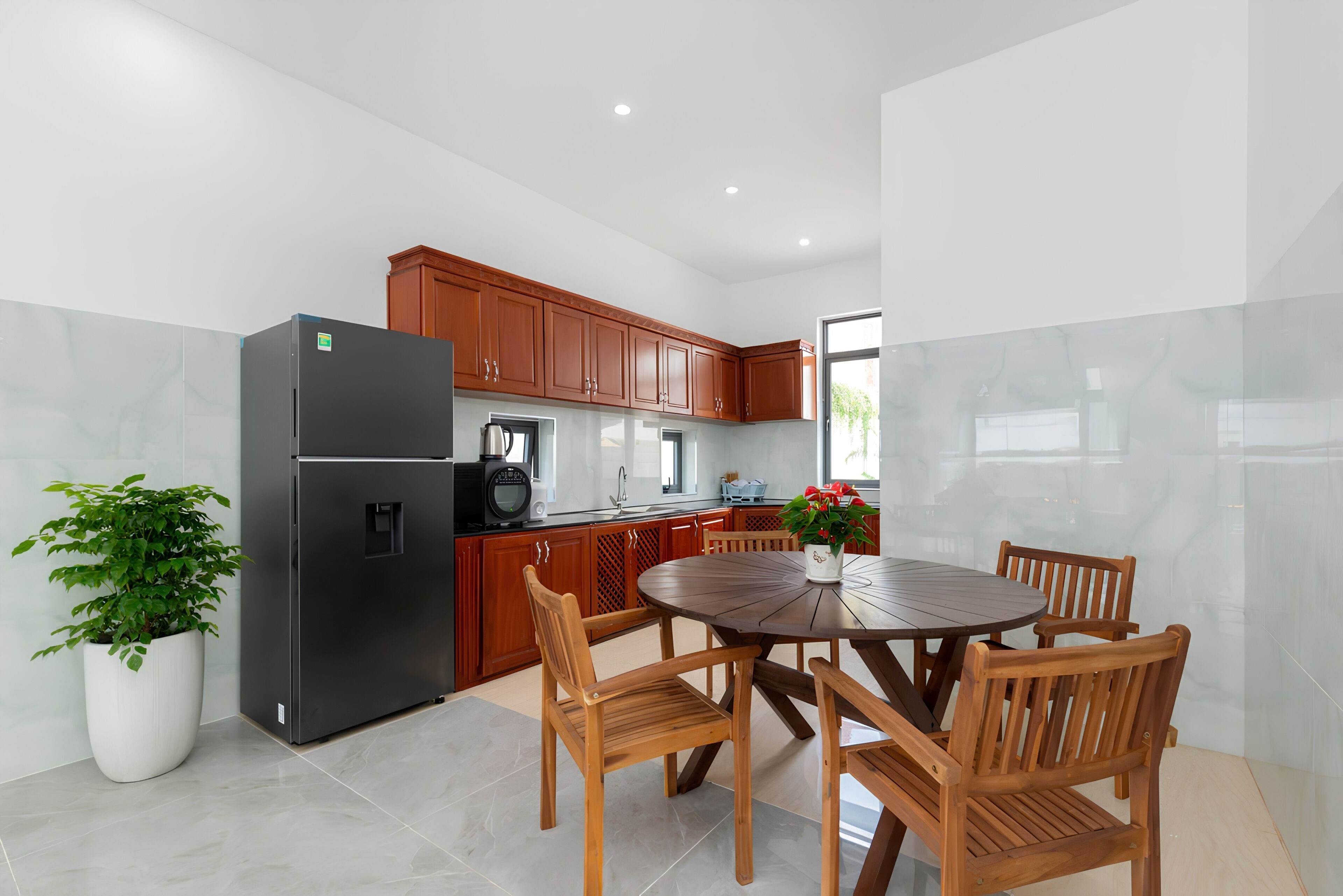 A modern kitchen with a dining area, featuring a refrigerator, stove, cabinets, and a round wooden table with chairs.