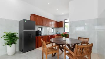 A modern kitchen with a dining area, featuring a refrigerator, stove, cabinets, and a round wooden table with chairs.