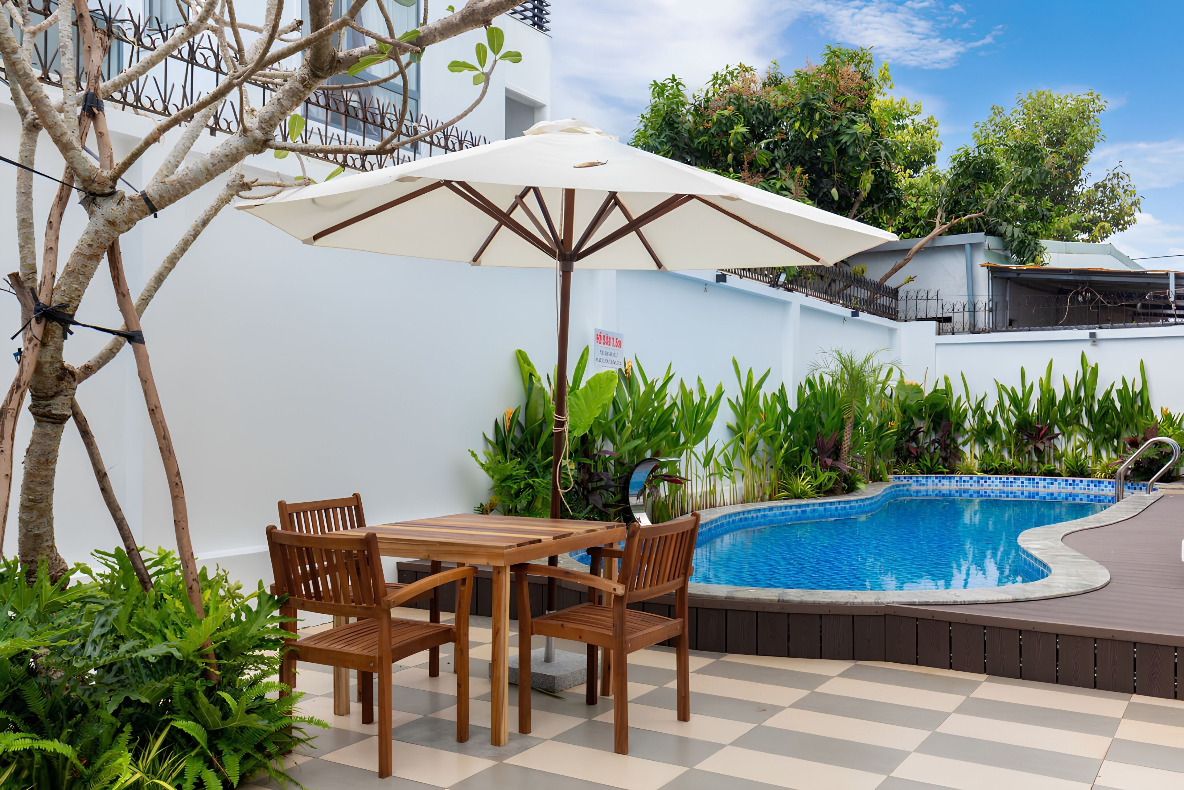 Un espace aménagé au bord de la piscine, avec une table et des chaises, entouré d’une végétation luxuriante et donnant sur une piscine à l’eau d’un bleu limpide.
